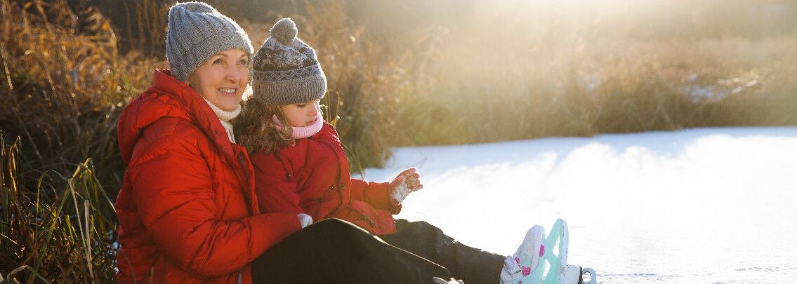 Grandma and grandchild in winter coats sitting in snow