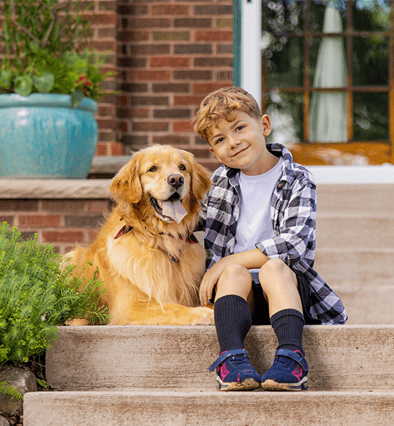 Boy in plaid shirt with golden retriever sitting outside of a home