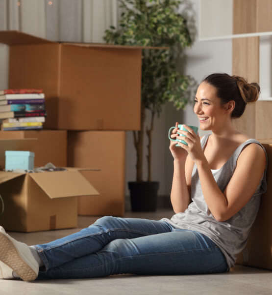 Women sitting by moving boxes sipping on coffee.