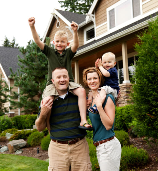 couple and their two kids standing outside of a two story home with beautiful green landscape.