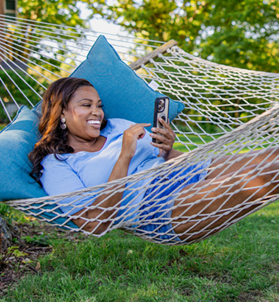 Women smiling at her phone sitting on hammock